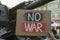 Woman holding poster with words No War near broken military tank on street, closeup