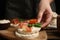 Woman holding puffed rice cake with prosciutto, tomato and basil at wooden table
