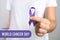 Woman holding purple ribbon against background, closeup. World Cancer Day