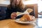 A woman holding and reading a book with a piece of croissant in a plate on wooden table