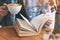 A woman holding and reading a vintage novel book while drinking coffee