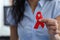 Woman holding red ribbon symbol in her hand.