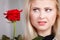 Woman holding red rose near face looking melancholic