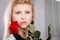 Woman holding red rose near face looking melancholic