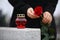 Woman holding red rose near grey granite tombstone with candle outdoors. Funeral ceremony