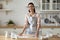 Woman holding rolling pin flattening dough looking at camera