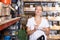 Woman holding shop list and choosing tools at shelves in build store