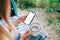 Woman holding a smartphone with a white screen mock up, sitting in a van and drinking tea during break in journey