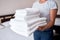 Woman holding stack of white clean bath towels in bedroom interior, copy space. Close up hands of hotel maid with towels.