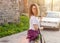 Woman holding straw bag with vivid bunch of lilac flowers walking down the street