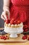 Woman holding summer sponge cake with fruits on ceramic cake sta