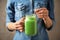 Woman holding tasty kale smoothie on brown background, closeup