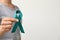 Woman holding teal awareness ribbon against light background