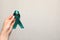 Woman holding teal awareness ribbon on grey paper, top view with space for text. Symbol of social and medical