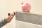 Woman holding thermostat near piggy bank on calorifer. Heating saving concept