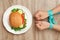 Woman holding tied hands near tasty sandwich on wooden table, top view. Healthy diet