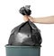 Woman holding trash bag full of garbage over bucket on white background, closeup