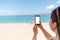 Woman holding up a smart phone at beach. Sea, sand and sky on the background. Concept of modern technology and internet. Copy