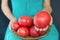 Woman holding a very large tomato, on her knees a basket with tomatoes.