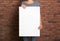 Woman holding white blank poster near red brick wall, closeup. Mockup for design