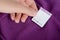 Woman holding white clothing label on purple garment, closeup