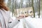 Woman holding wooden board with handwritten letters, snowy road through the forest in the background