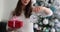 Woman holds alarm clock and gift against Christmas tree