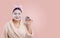 Woman holds cosmetics jar containing facial mask in her hand. Pink background adds touch of elegance and feminine energy