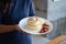 A woman holds a dish of two layers of puffy souffle pancakes in white dish with icing sugar, butter, whipped cream and mixed fresh