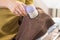 The woman holds an electric shaver in her hand to clean mottled clothes and cleans the sleeve of a brown wool sweater.