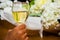 Woman holds in her arm a glass of white wine over a background of bouquet of artificial flowers