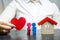 A woman holds in her hands a red heart near a miniature family and home. The concept of property insurance and house. Home