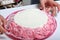 A woman holds in her hands an unfinished cake, decorated with a cream of pink color