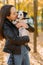 Woman holds and kisses puppy of dalmatian dog in autumn park