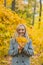 A woman holds maple yellow leaves in her hands in a park against a background of trees, going to throw up a pile of leaves