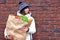 Woman holds paper bag of vegetables and food from grocery store on brick wall background. Girl with paper package of food.