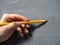 A woman holds a pencil in her left hand on a gray textured background. The concept of the artist, left-handed