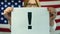 A woman holds a poster with a exclamation mark against the background of the American flag