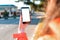 A woman holds a smartphone in her hand, hand close-up. In the background, the city road is blurred. Mock up. Concept of modern