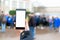 A woman holds a smartphone in her hand, people in the background are blurred. Outdoor. Close up. Mock up. The concept of