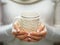 Woman holds a winter cup close up. Woman hands with elegant french manicure nails design holding a cozy knitted mug.