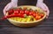 A woman holds a wooden plate with macaroni, cherry tomatoes and red pepper in her hands. Rustic natural organic food.