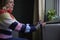 Woman At Home In Gloves Warming Hands By Radiator During Cost Of Living Energy Crisis