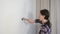 Woman house painter is painting wall using brush doing renovation at home.