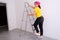 Woman house painter takes a step on ladder on white wall background