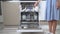 A woman housewife loads the top shelf of the dishwasher with dirty plates and mugs front view close-up