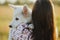 Woman hugging cute white puppy in warm sunset light in summer meadow, back view. Happy girl holding adorable fluffy puppy close up