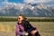 Woman hugs and holds her black labrador retriever dog in front of the Grand Teton National Park mountains in Jackson Wyoming as