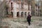 A woman in the image of Baron Saturday poses against the backdrop of an old ruined brick building. The model is wearing