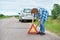 Woman installing emergency sign on road near car